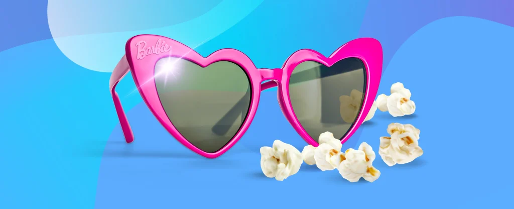 An illustrated pair of pink barbie sunglasses in the shape of love hearts sits behind popcorn, set against a blue background.